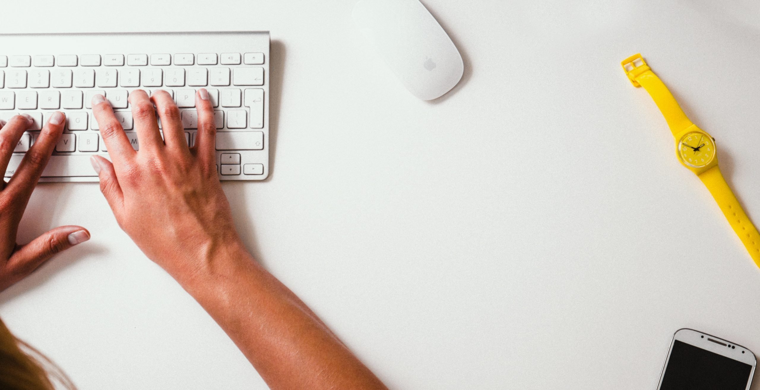 mãos digitando em um teclado de computador branco, com um mouse branco ao lado