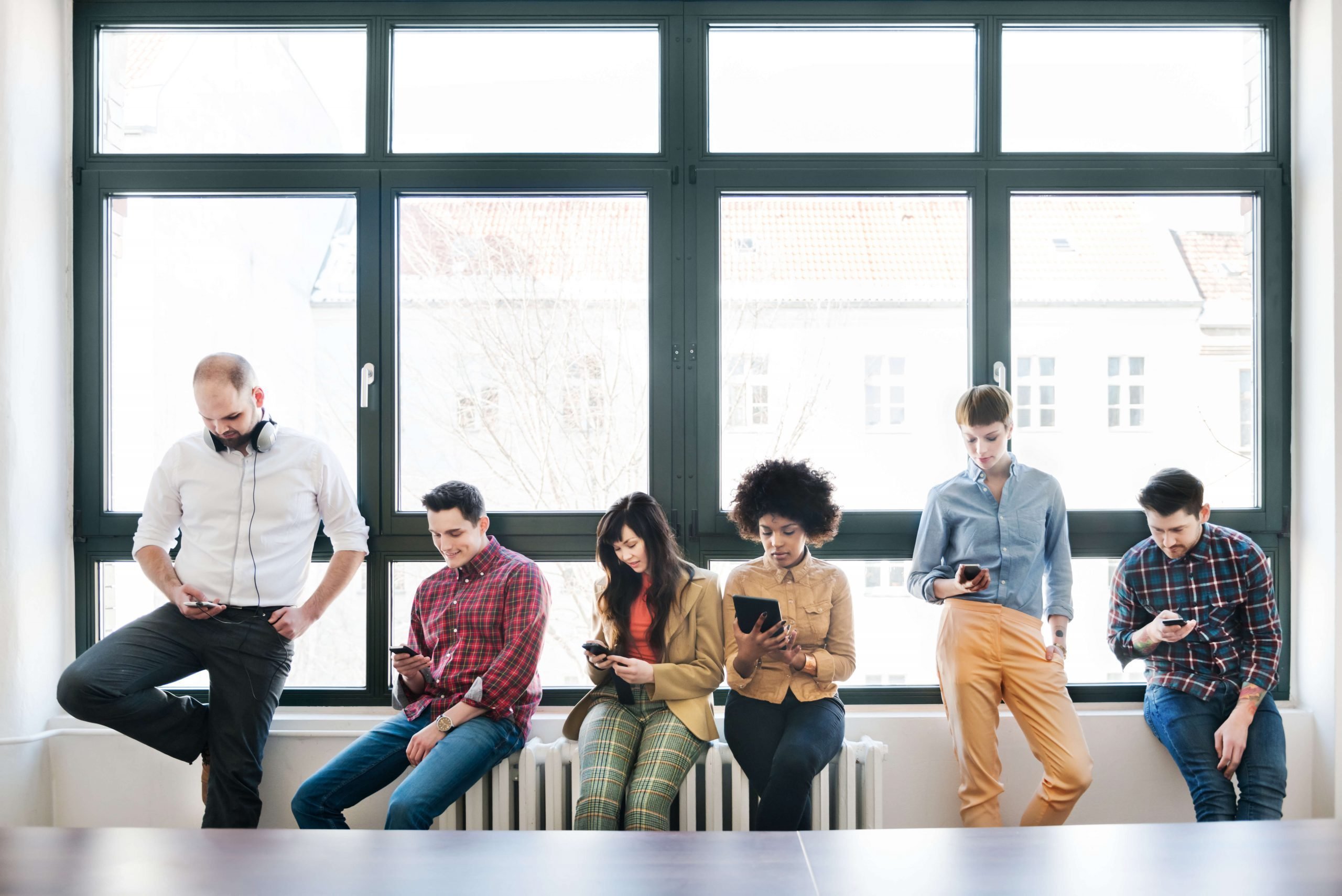 grupo de jovens, composto por homens e mulheres de diversas etnias, estudando em seus smatphones