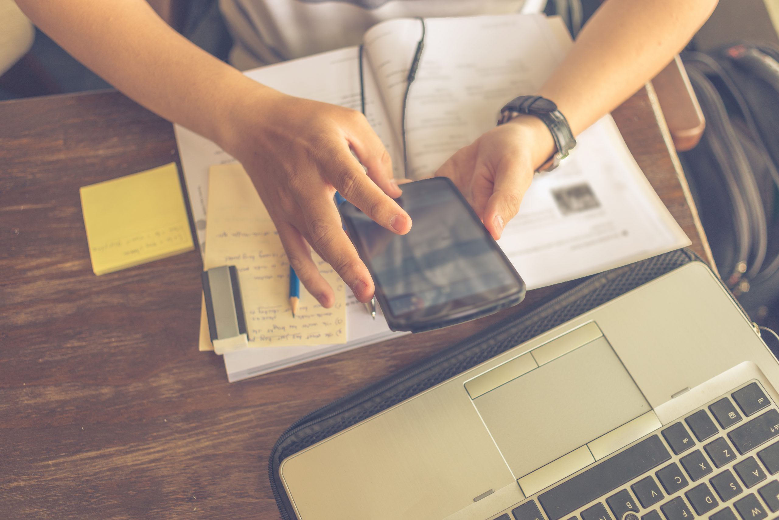 mãos usando um smartphone sobre uma mesa com livros e notebook