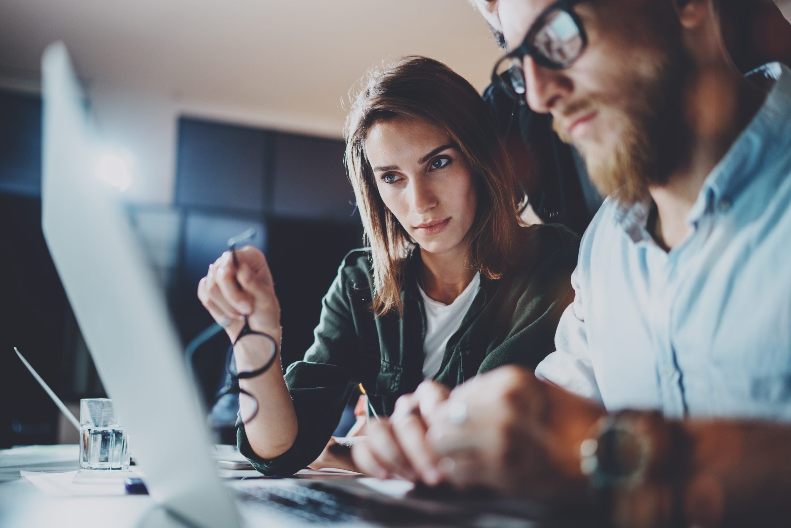 dois profissionais, homem e mulher jovens, analisando um projeto no notebook e discutindo a respeito