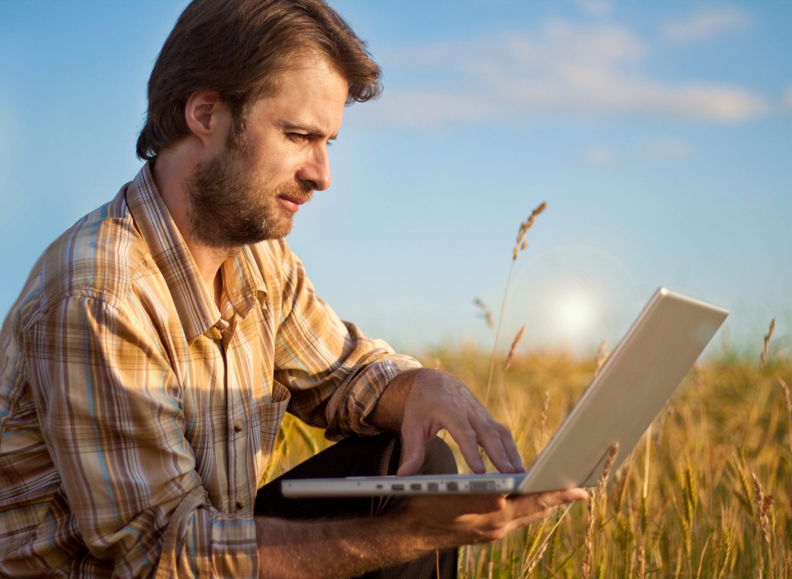 profissional do campo utilizando um notebook em meio à uma plantação